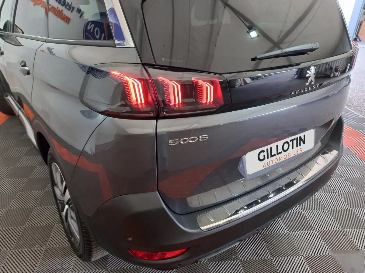 Vue 3/4 arrière droite d'un Peugeot 5008 gris foncé avec feux arrière LED allumés et logo visible.