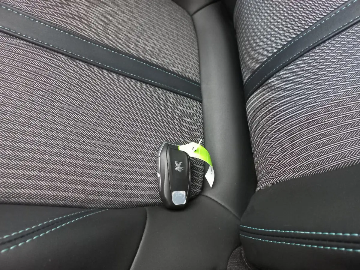 Gros plan sur la clé Peugeot posée sur un siège tissu gris à motifs chevrons avec surpiqûres bleues.