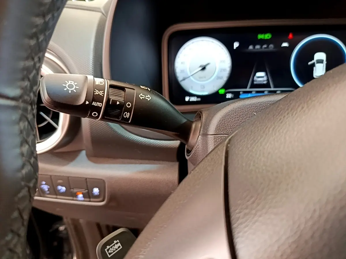 Vue intérieure centrée sur le volant cuir et la commande des feux, avec tableau de bord numérique du Hyundai Kona bleu 2023.