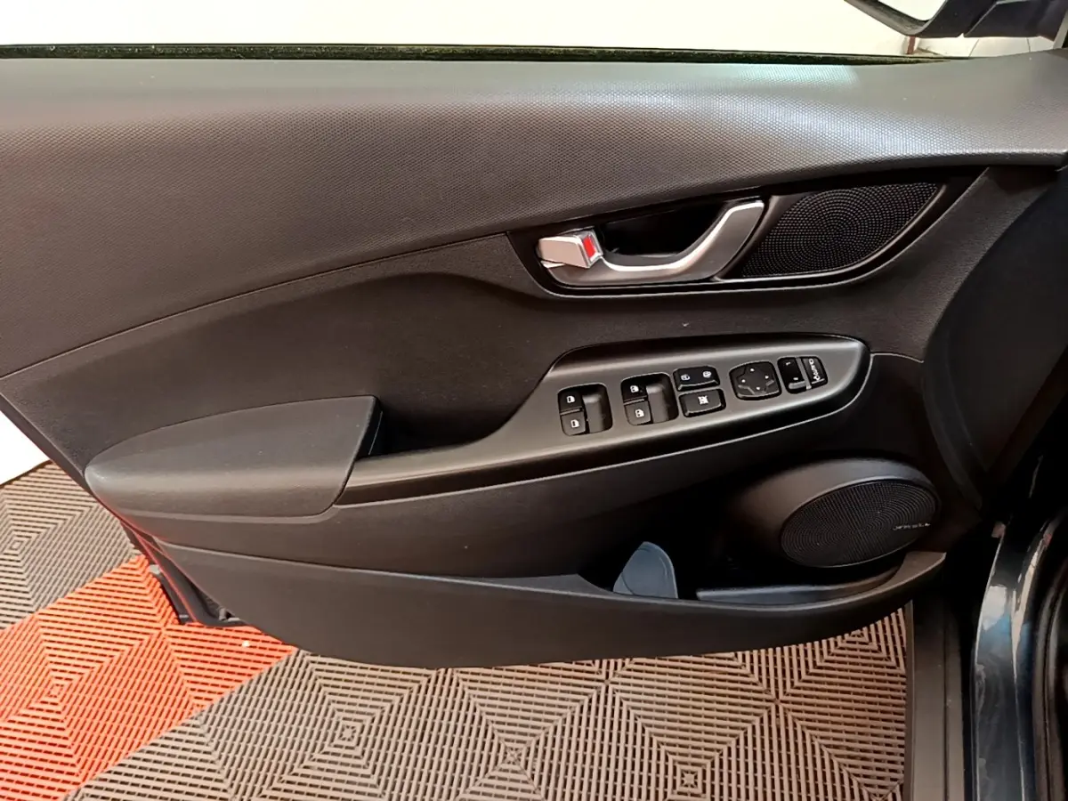 Vue rapprochée de la porte avant gauche intérieure noire avec commandes électriques et haut-parleur Hyundai Kona 2023.