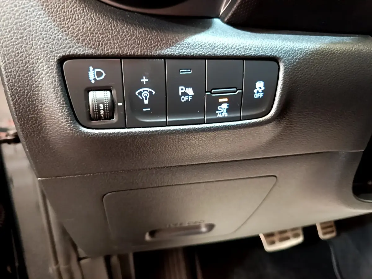 Vue rapprochée des commandes d’aide à la conduite et réglages lumineux sur la gauche du tableau de bord d’une Hyundai Kona électrique.