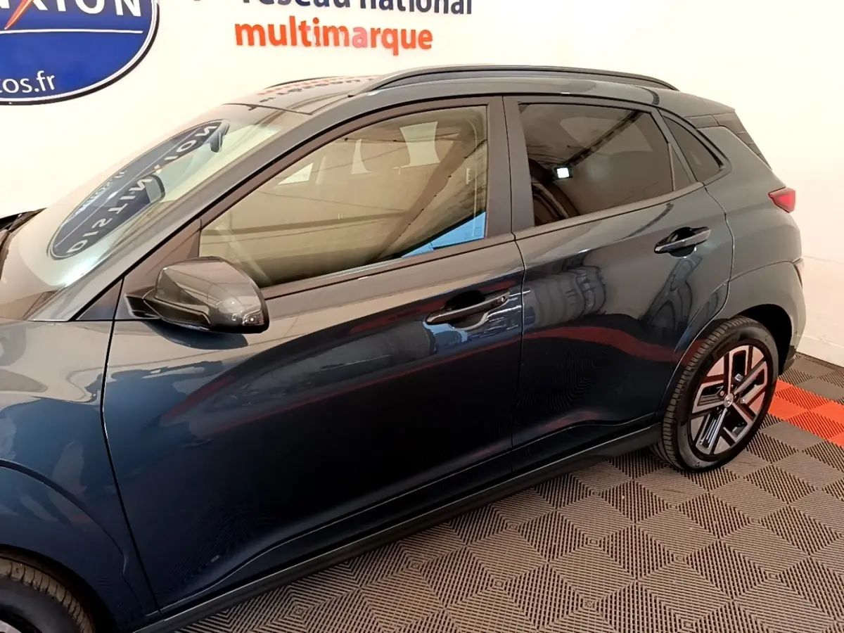 Vue latérale gauche d’un Hyundai Kona électrique bleu avec jantes distinctives et rétroviseurs noirs rabattables.