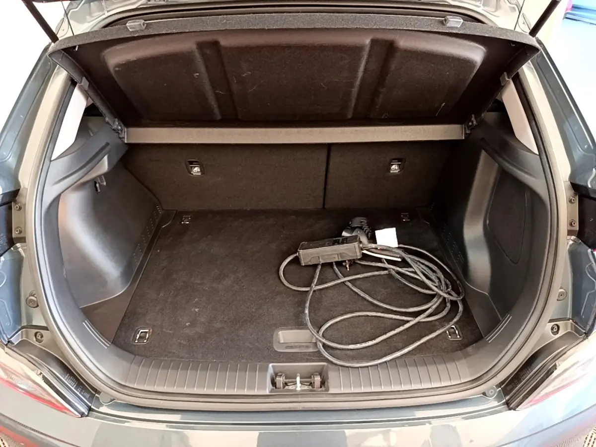 Vue arrière du coffre ouvert d’une Hyundai Kona électrique bleu avec câble de charge visible à l’intérieur.
