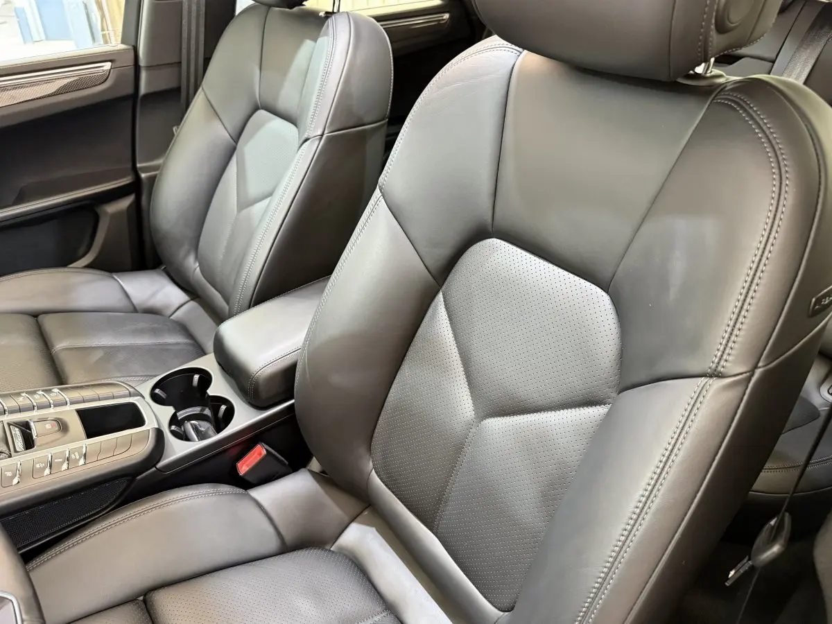 Gros plan sur les sièges avant en cuir gris foncé du Porsche Macan 3.0 S, avec console centrale et accoudoir visibles.