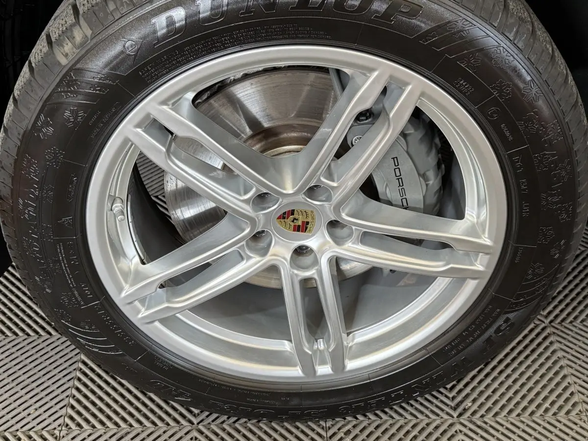 Gros plan sur la jante alu argentée avec logo Porsche et pneu Dunlop du Porsche Macan 3.0 S gris foncé.