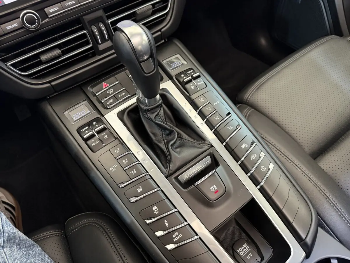 Gros plan sur la console centrale cuir noire du Porsche Macan 3.0 S avec levier de vitesse et commandes climatisation.