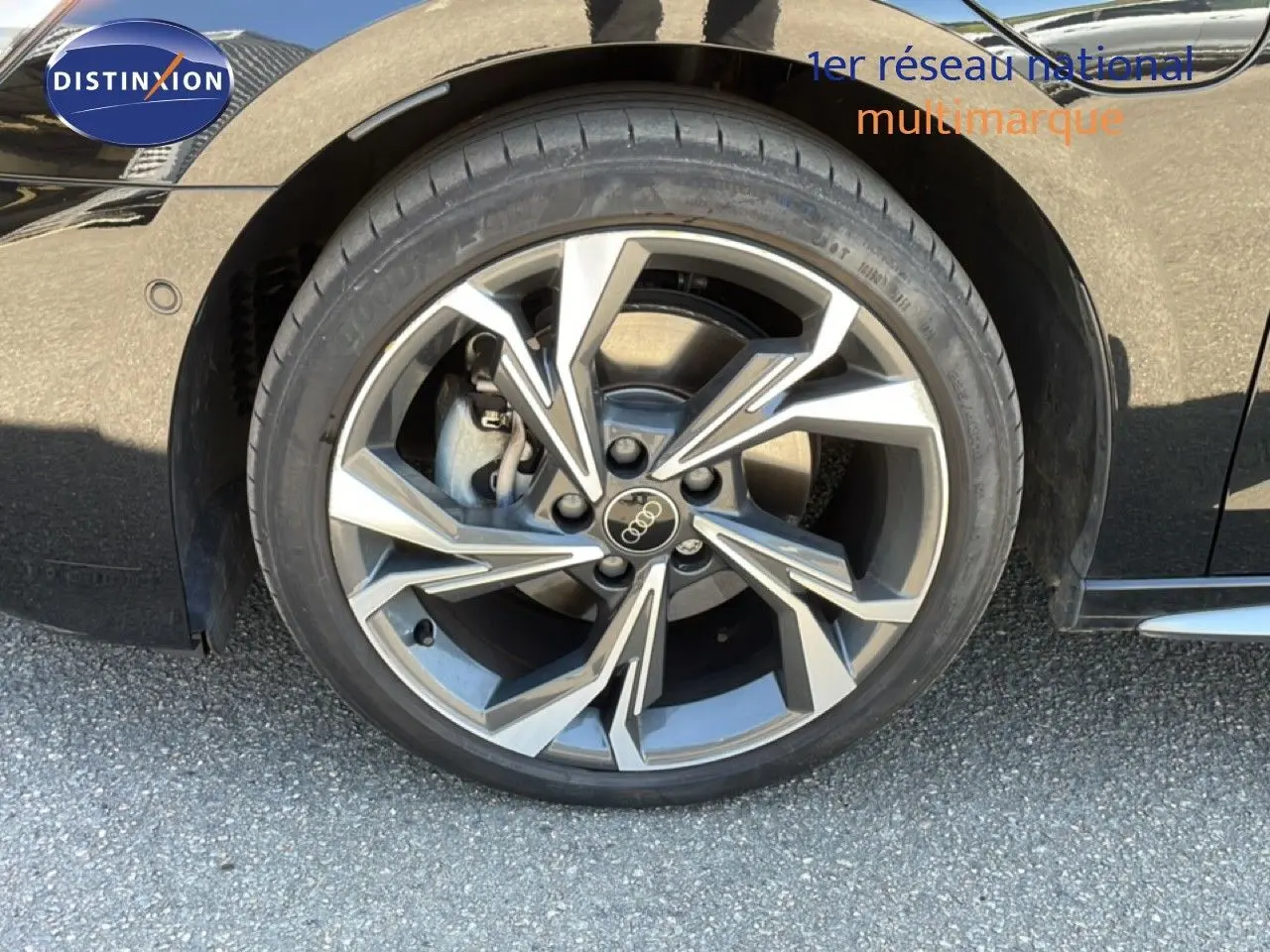 Gros plan sur la roue avant droite d'une Audi A3 Sportback noire, mettant en valeur la jante alliage à design moderne.