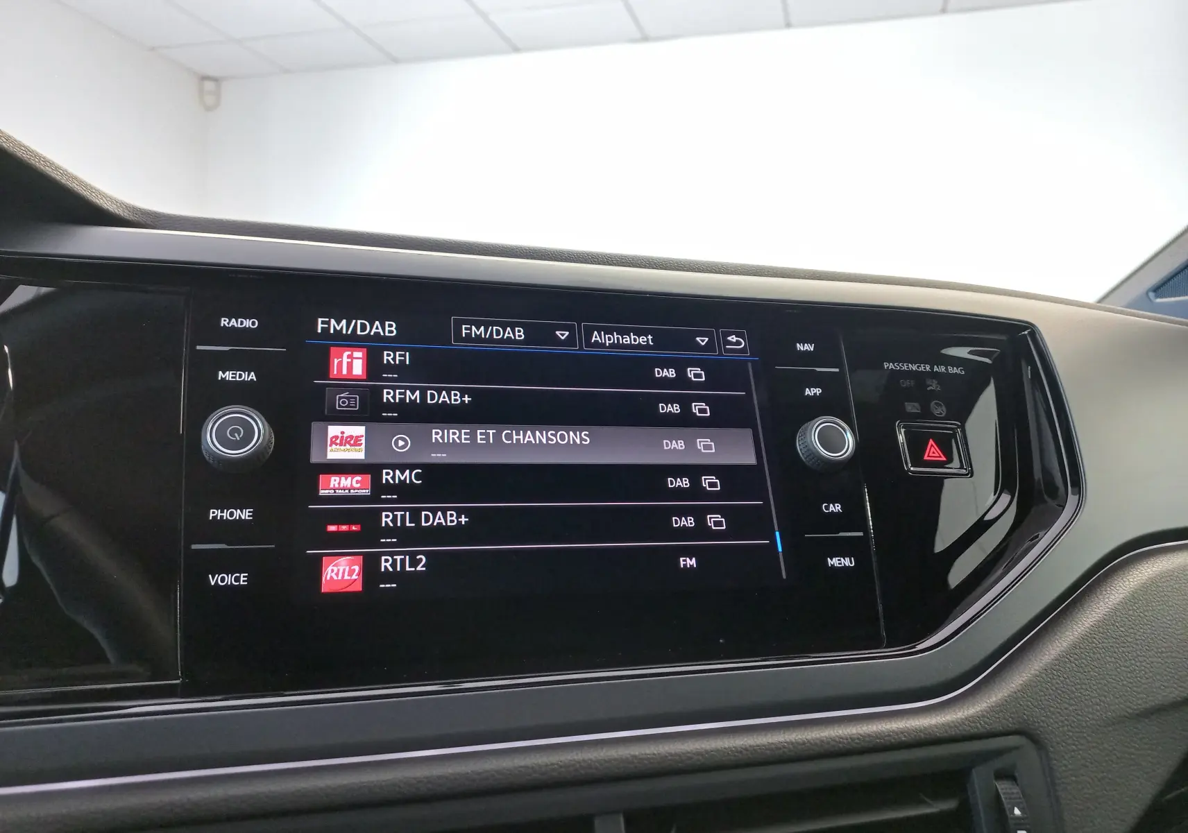 Écran tactile central de la Volkswagen Polo 2025 Rouge Roi, affichant les stations radio FM/DAB avec commandes autour.