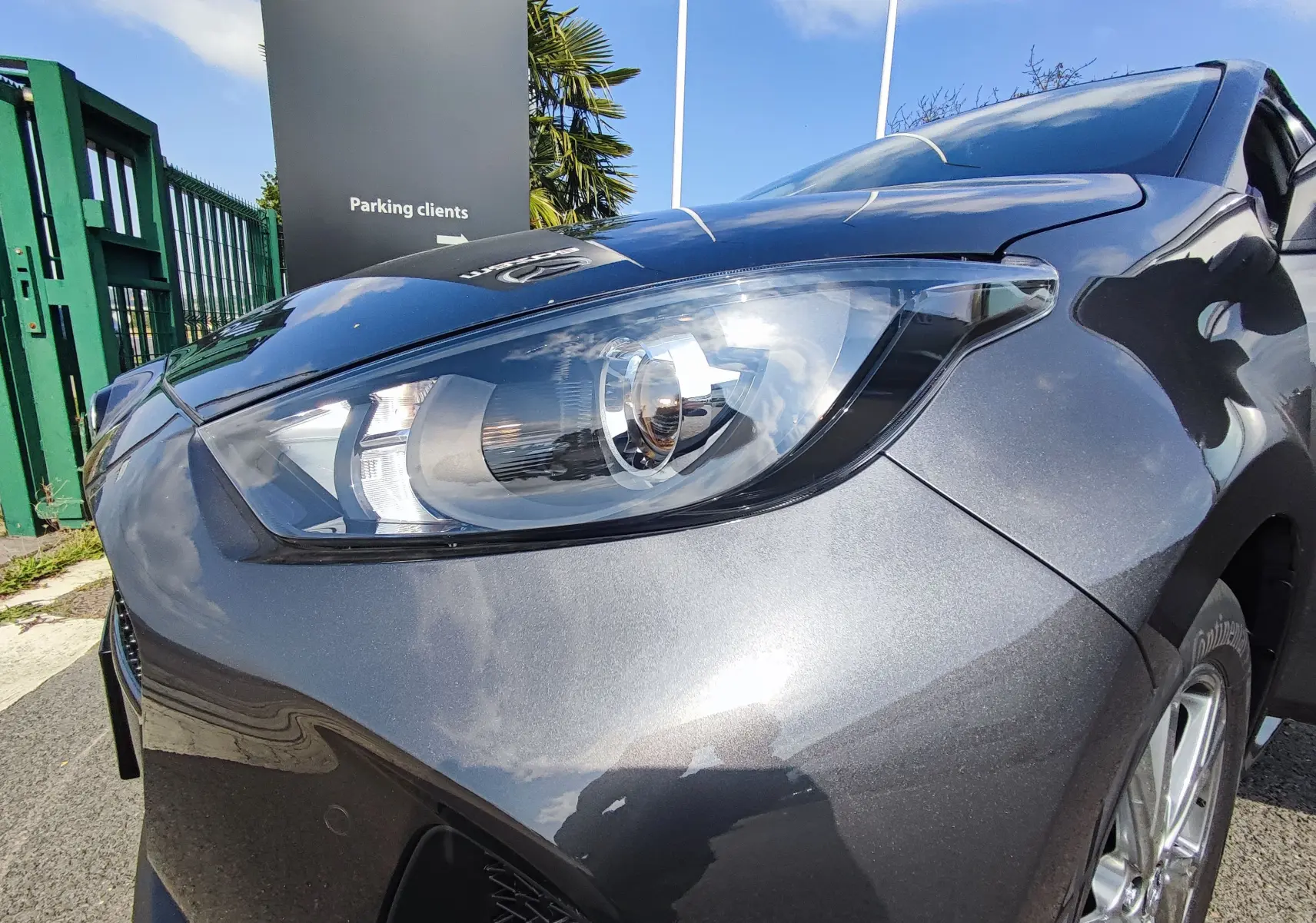 Gros plan sur le phare avant gauche d'une Mazda2 gris foncé 2024, soulignant la finition brillante et les détails du capot.