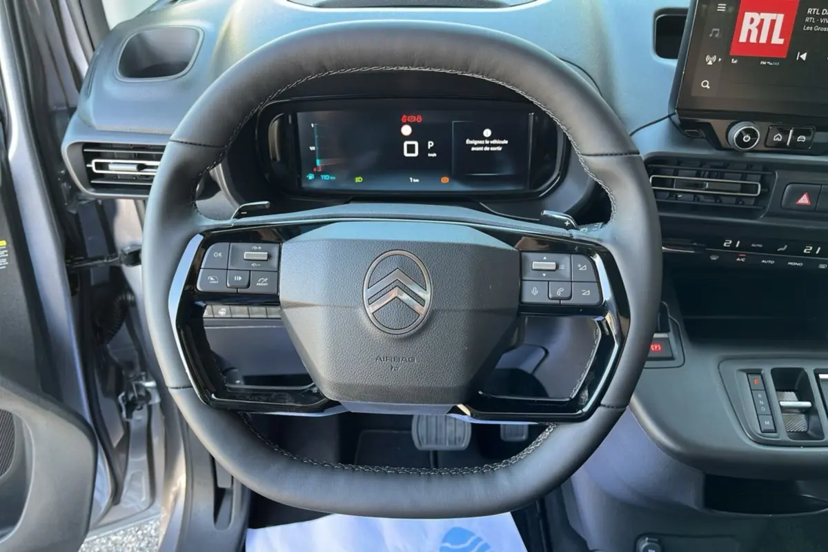 Vue intérieure centrée sur le volant du Citroën Berlingo 2025 gris artense avec tableau de bord digital et commandes intégrées.