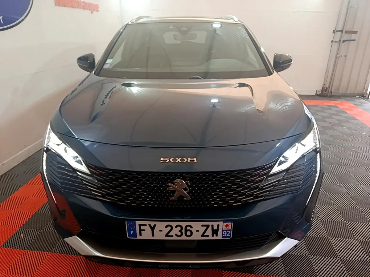 Vue frontale d'un Peugeot 5008 bleu 2021 avec calandre noire et phares LED allumés dans un garage.