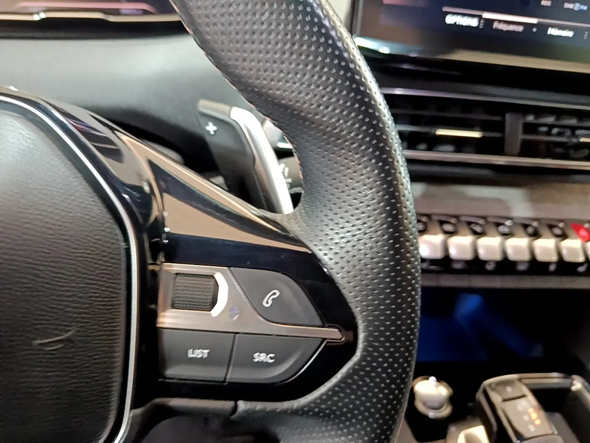 Gros plan sur le volant cuir perforé côté gauche du Peugeot 5008 Bleu, avec commandes audio et téléphone intégrées.