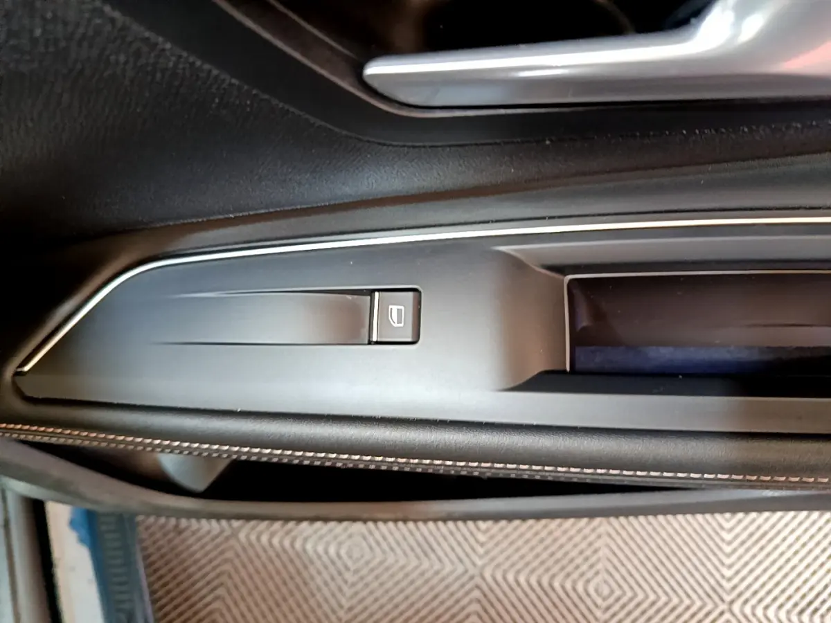 Gros plan sur la commande de lève-vitre en plastique noir mat, sur la porte intérieure côté conducteur du Peugeot 5008 bleu.