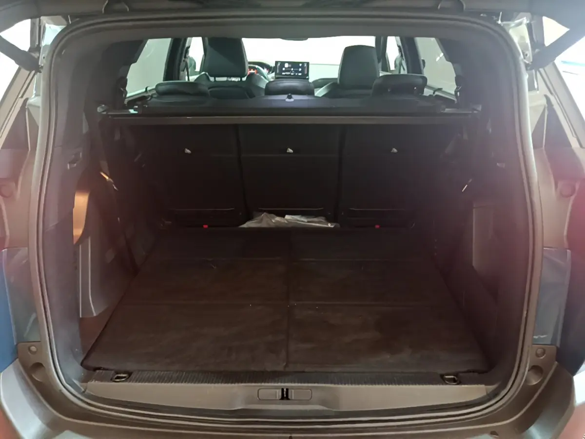 Coffre ouvert vu de l'arrière du Peugeot 5008 bleu, montrant la banquette rabattue et l'intérieur spacieux.