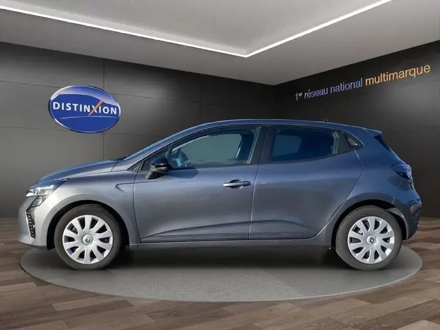 Profil droit de la Renault Clio V gris schiste 2024 avec enjoliveurs 16 pouces dans un showroom intérieur.
