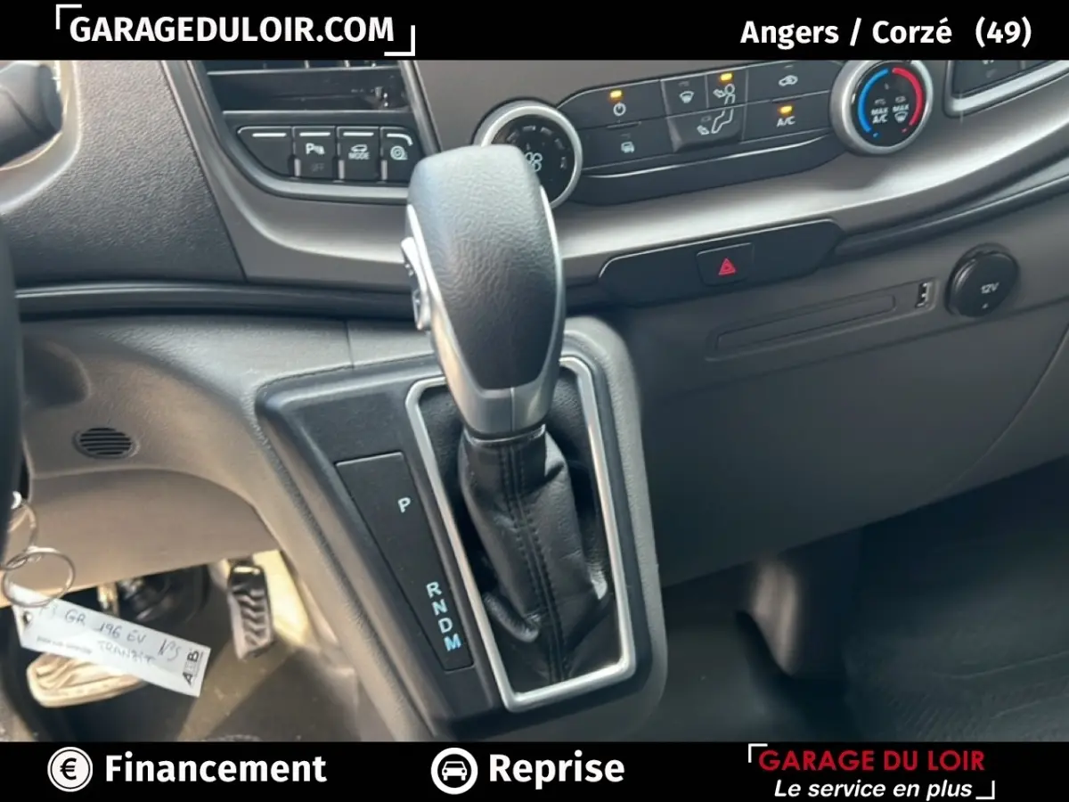 Gros plan sur la console centrale du Ford Transit Custom blanc, mettant en valeur le levier de vitesses automatique et les commandes climatisation.