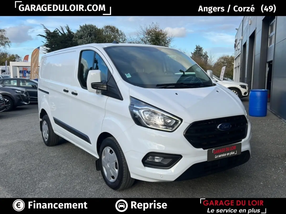 Vue 3/4 avant droit d'un Ford Transit Custom fourgon blanc avec calandre noire et feux LED, stationné en extérieur.