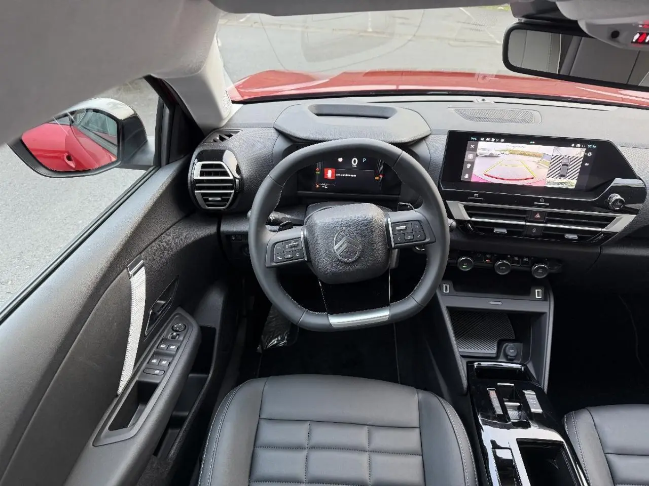 Vue intérieure avant du Citroën C4 rouge elixir 2025, tableau de bord avec écran tactile et volant multifonction.