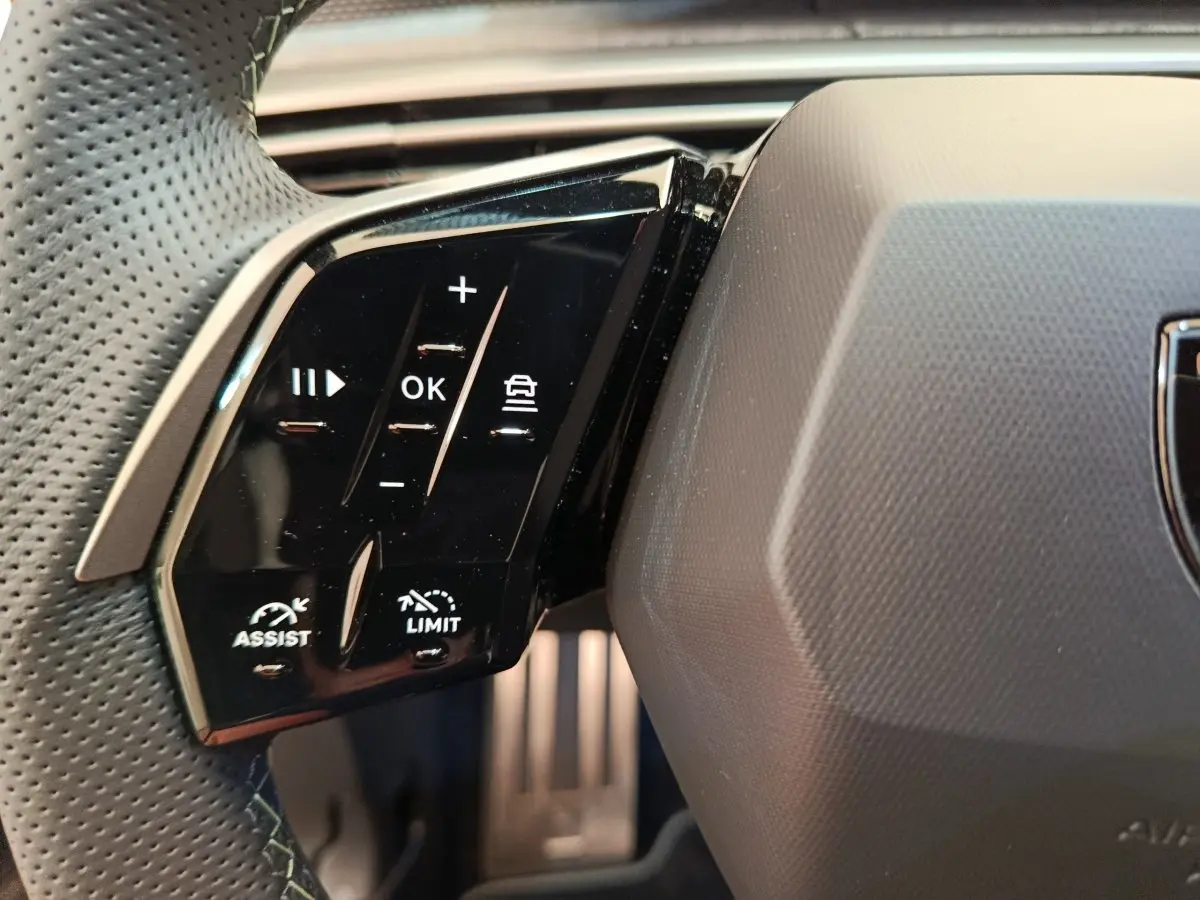 Gros plan sur les commandes multifonctions à gauche du volant cuir perforé du Peugeot 3008 gris clair 2025.