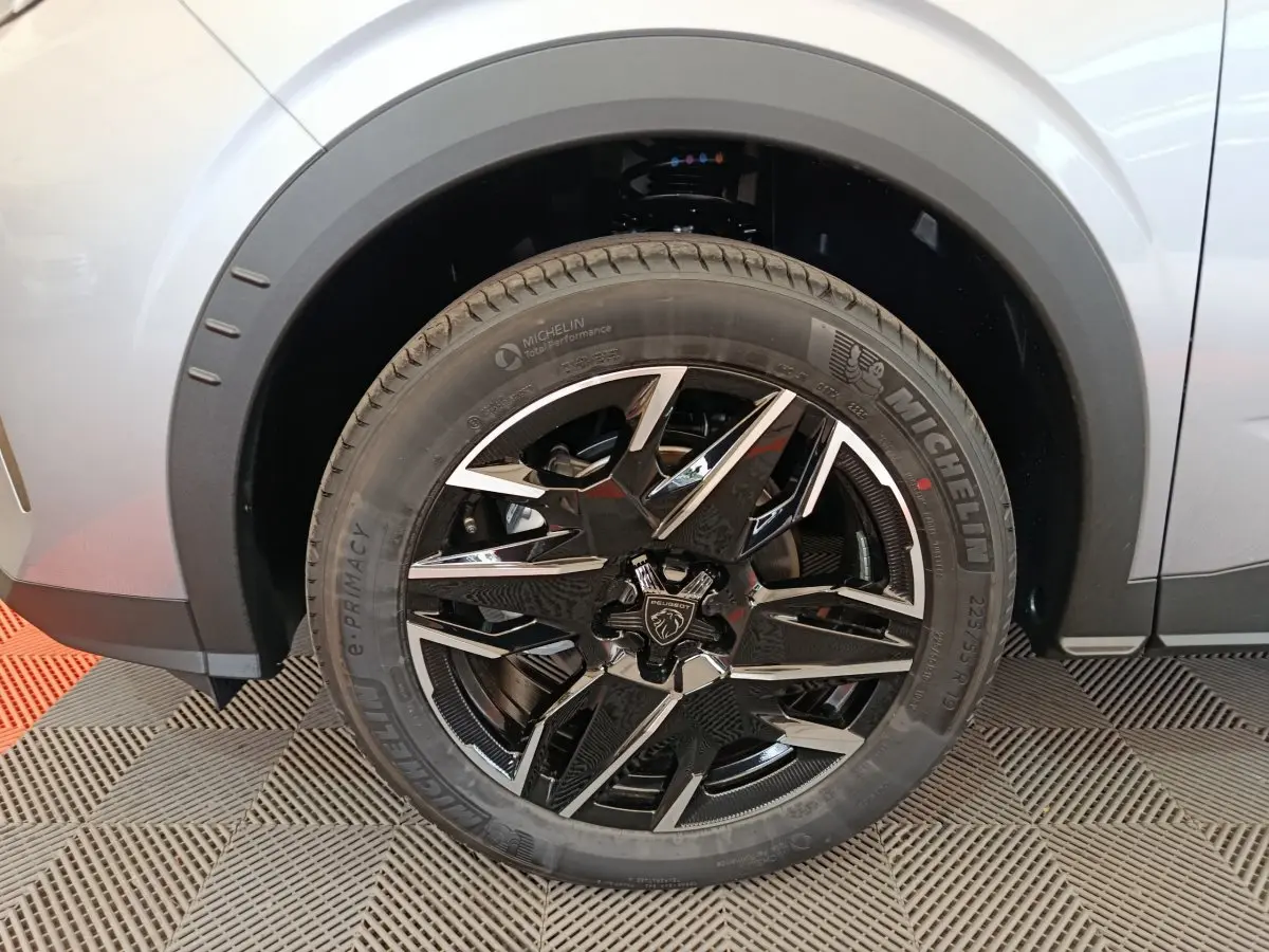 Gros plan sur la roue avant gauche du Peugeot 3008 gris clair, jante alliage noire et argent avec logo lion central.