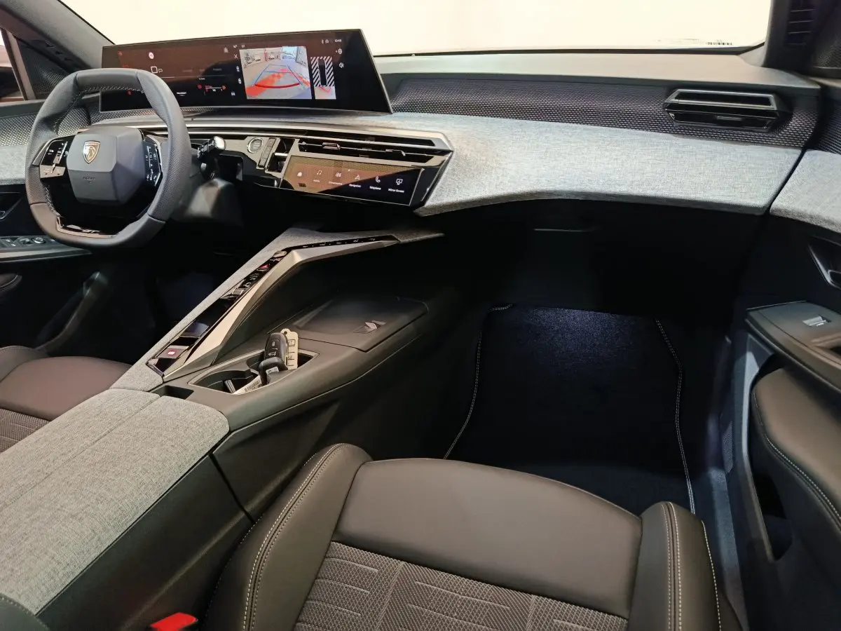 Intérieur du Peugeot 3008 2025, vue côté passager, tableau de bord gris clair avec écran tactile large et volant cuir noir.