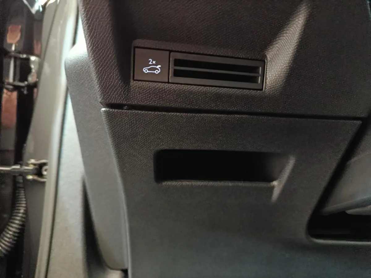 Gros plan sur le bouton d'ouverture du coffre dans l'habitacle noir du Peugeot 3008 gris clair hybride 2025.