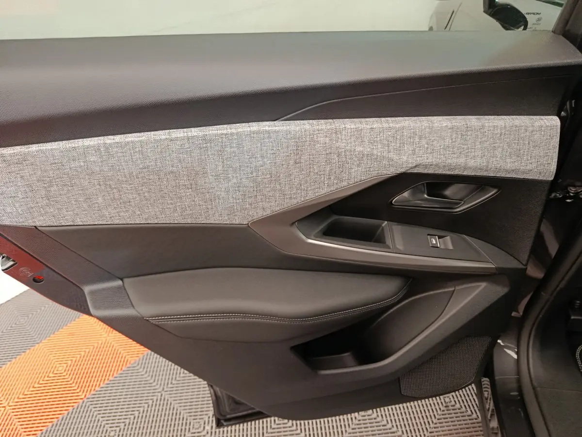 Gros plan sur la porte intérieure côté gauche du Peugeot 3008 gris clair, avec habillage tissu et cuir noir.