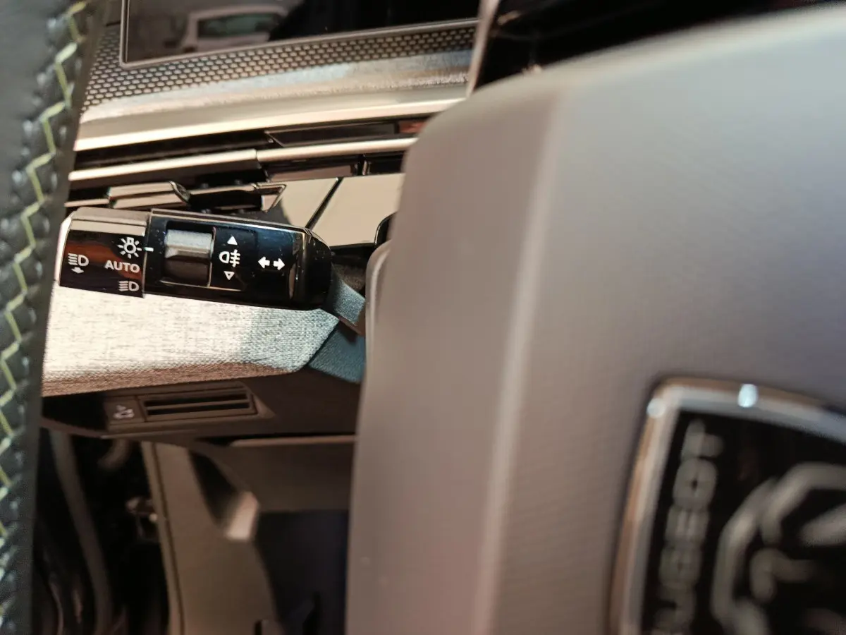 Gros plan sur la manette des feux à gauche du volant gris du Peugeot 3008 hybride 2025, intérieur moderne.