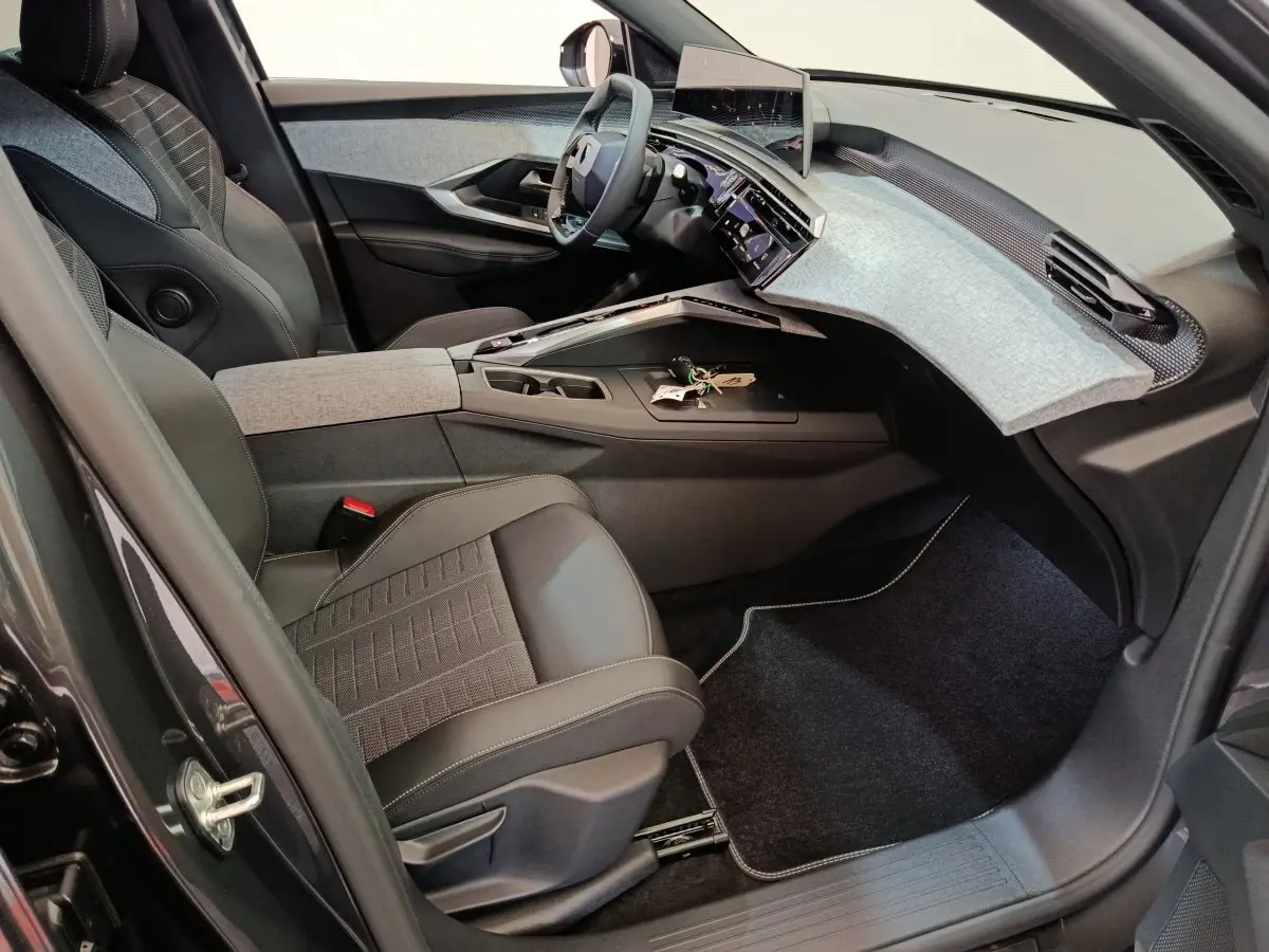 Vue intérieure côté conducteur du Peugeot 3008 gris clair 2025, avec tableau de bord moderne et sièges en tissu et cuir.