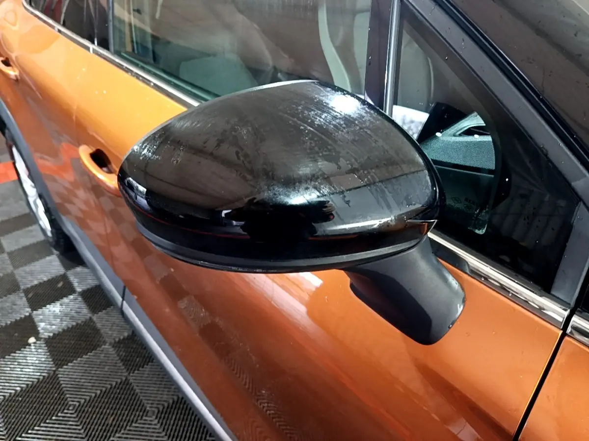 Gros plan sur le rétroviseur noir côté conducteur d’un Renault Captur jaune vu de profil gauche.