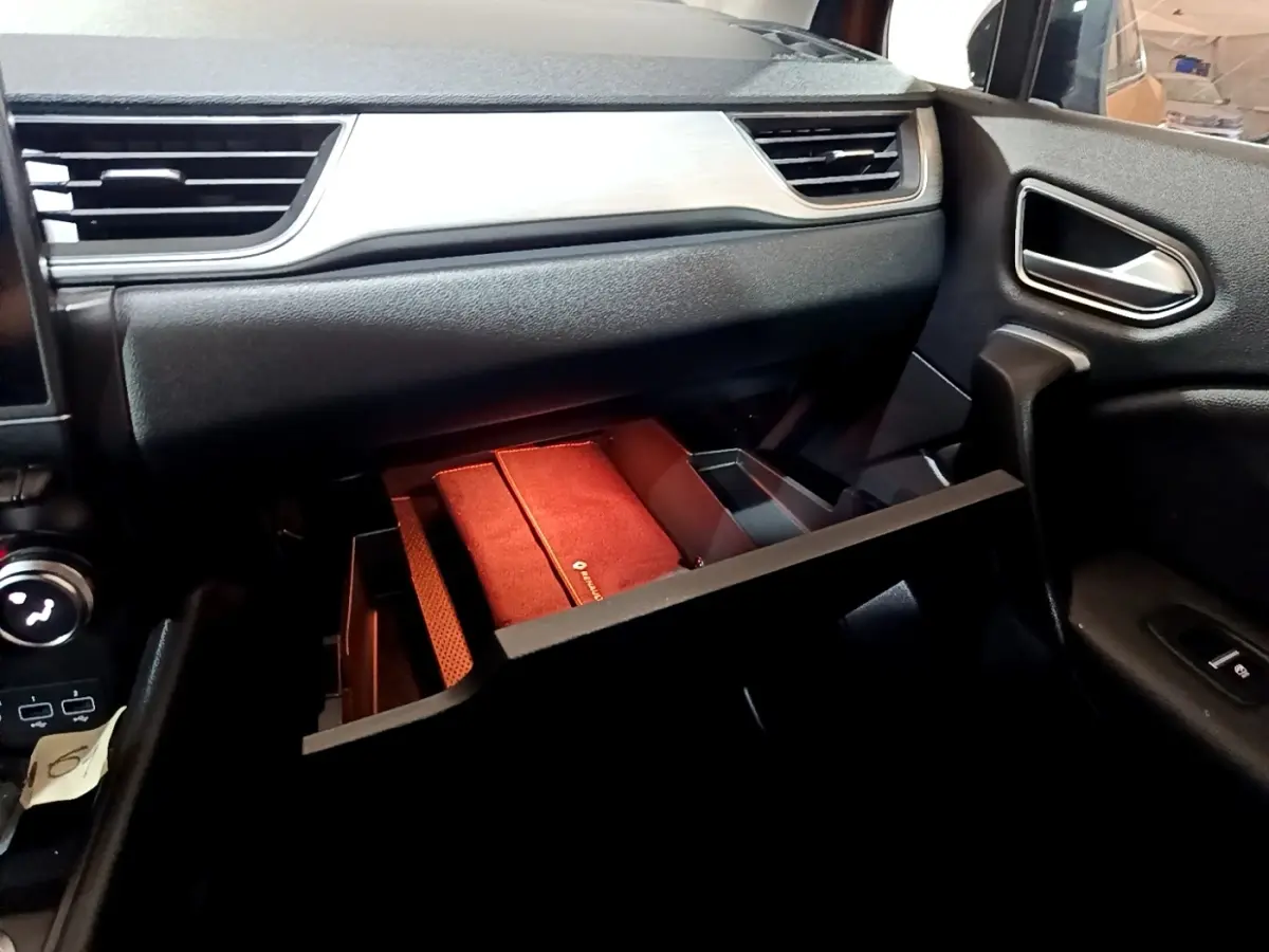 Vue intérieure côté passager du tableau de bord noir du Renault Captur Intens avec boîte à gants ouverte et rangement rouge visible.