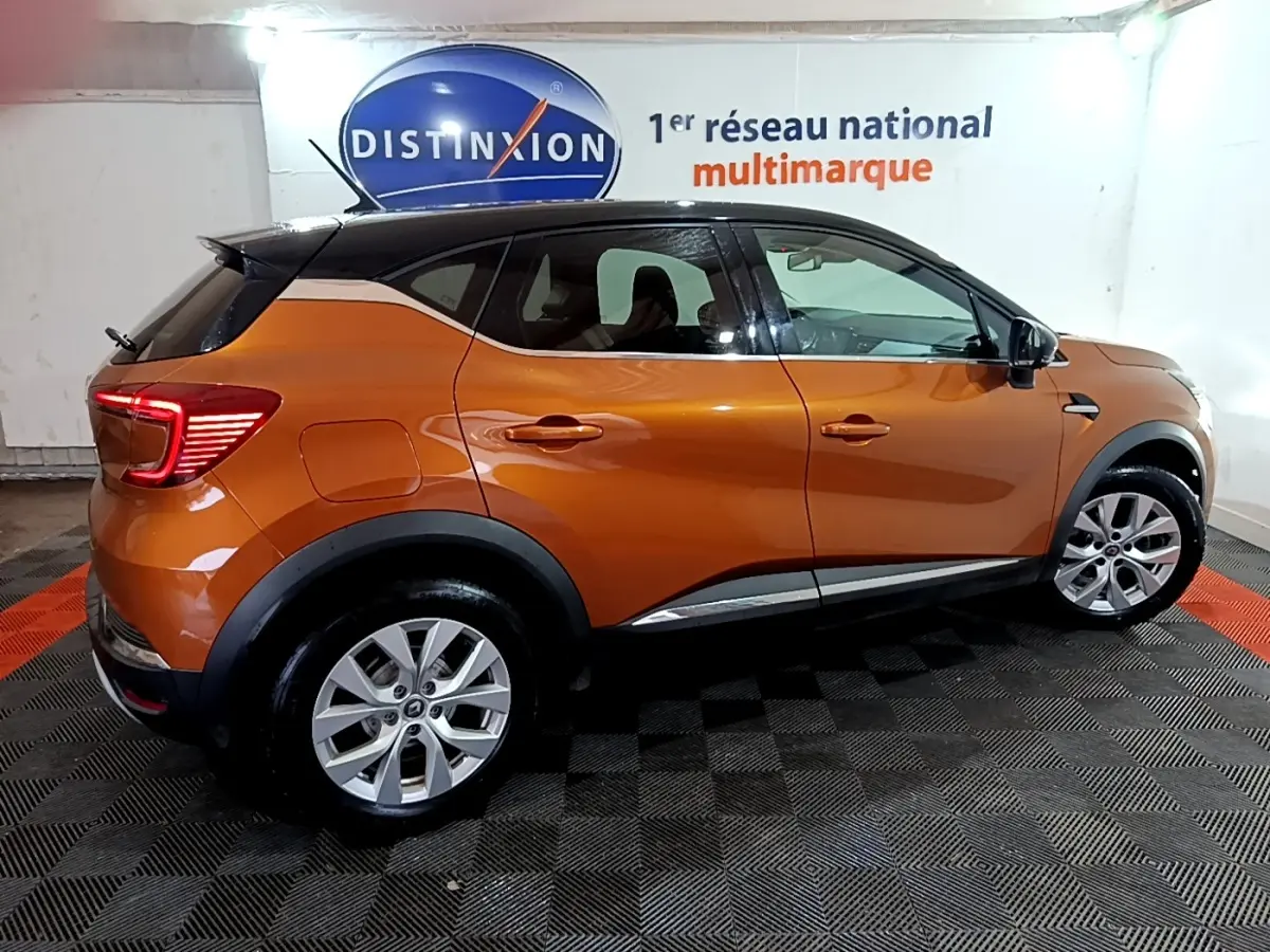 Vue de profil côté droit d'un Renault Captur jaune orangé 2020 dans un showroom avec jantes alliage et feux arrière LED allumés.