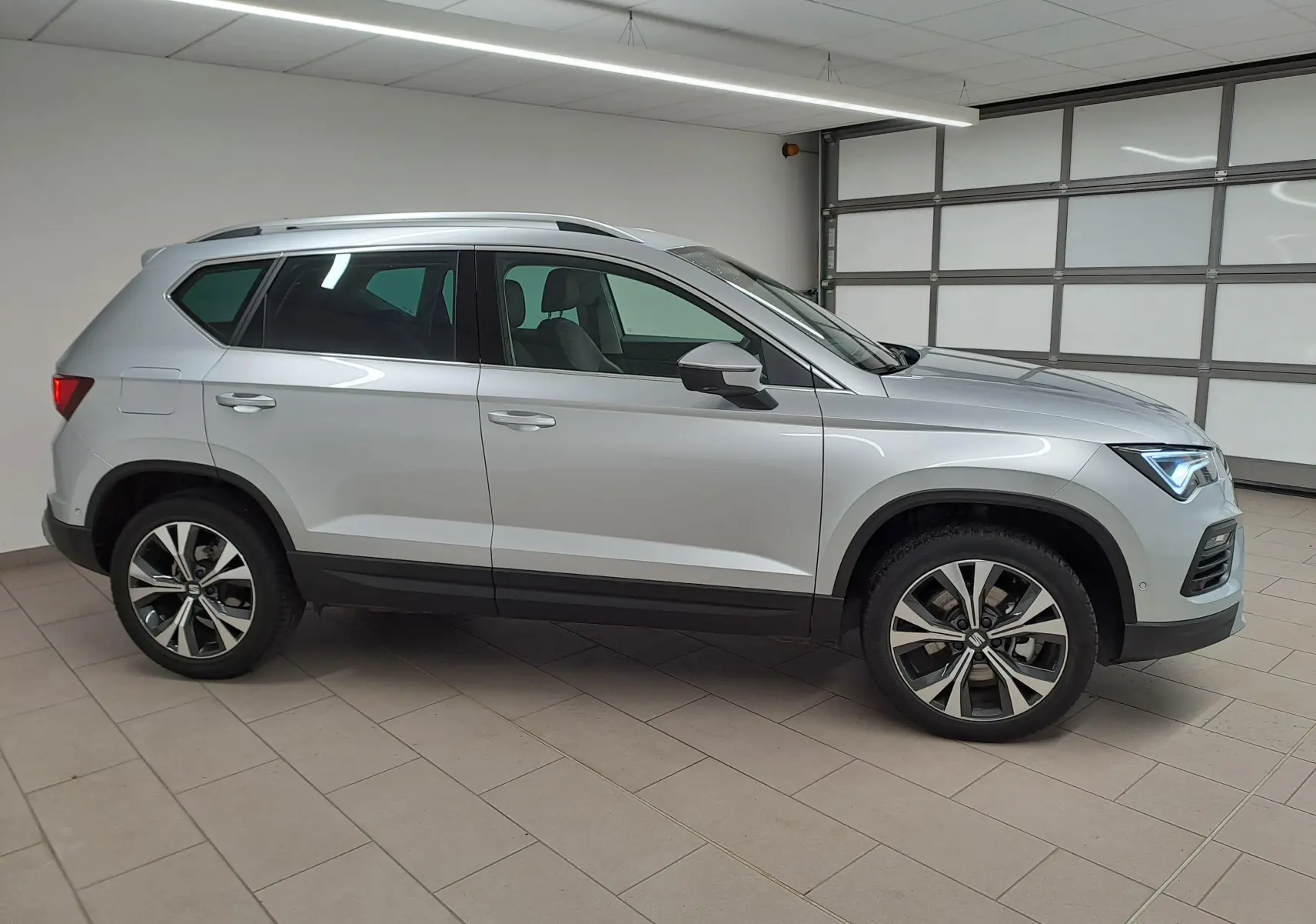 Vue de profil côté gauche d'un SEAT Ateca 2025 argent métallisé avec jantes alliage 18 pouces dans un garage.