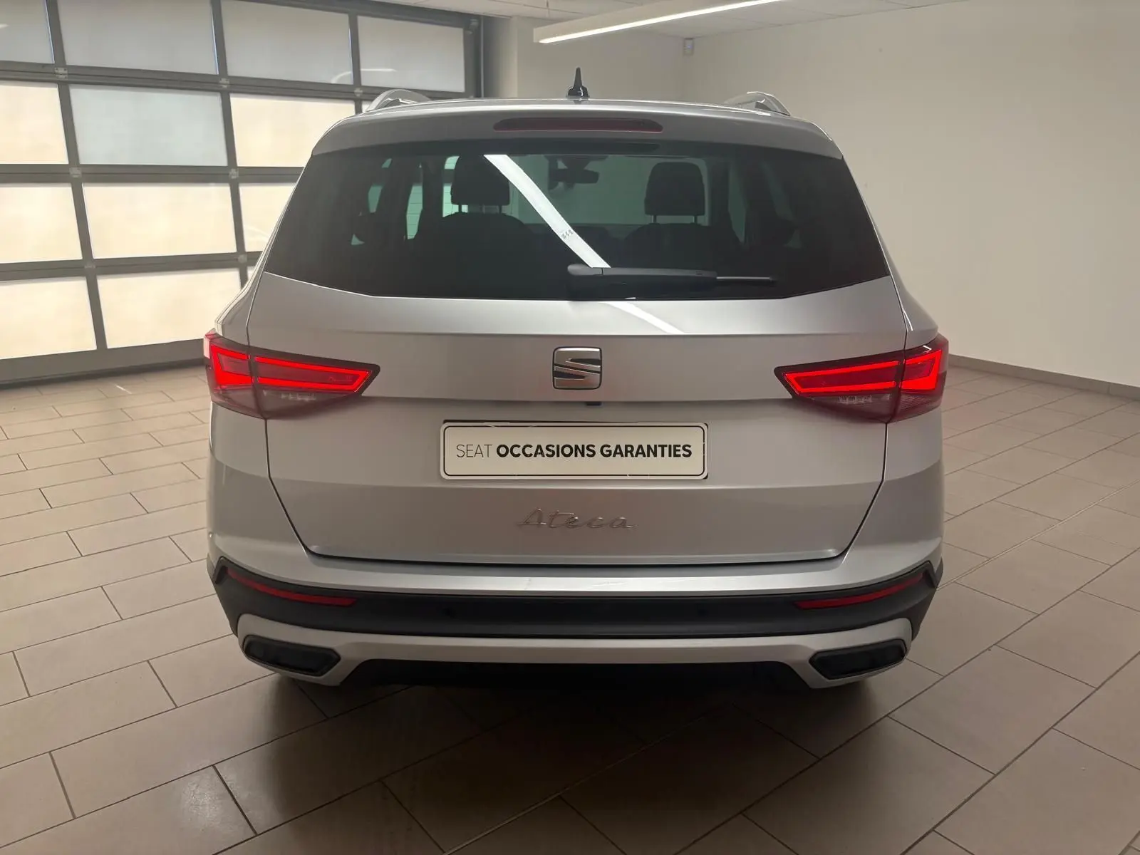 Vue arrière d'un SEAT Ateca 2025 argent métallisé avec feux LED allumés et hayon électrique en intérieur showroom.