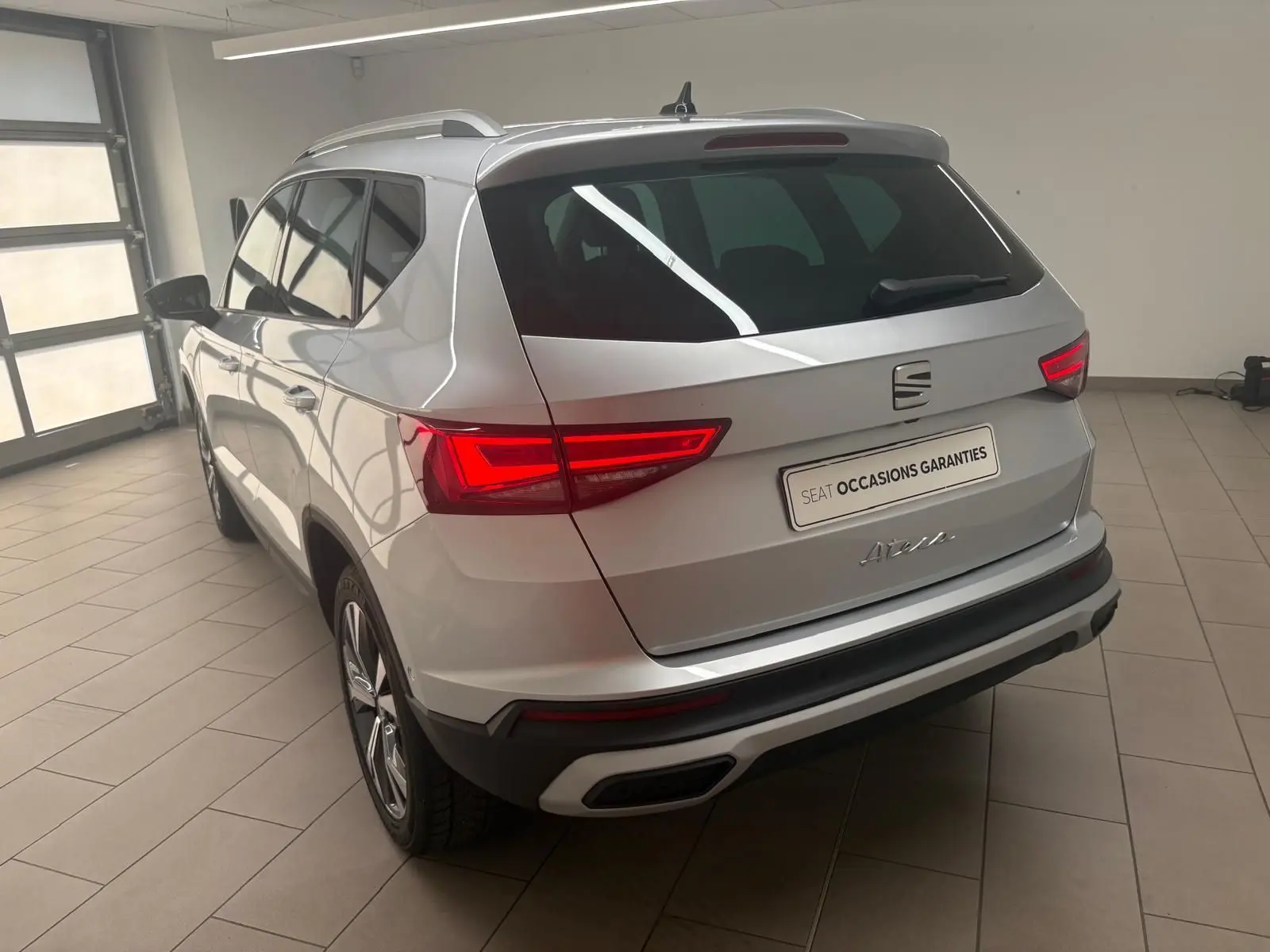Vue 3/4 arrière droite d'un SEAT Ateca 2025 argent métallisé avec jantes alliage 18'' et hayon électrique mains-libres.