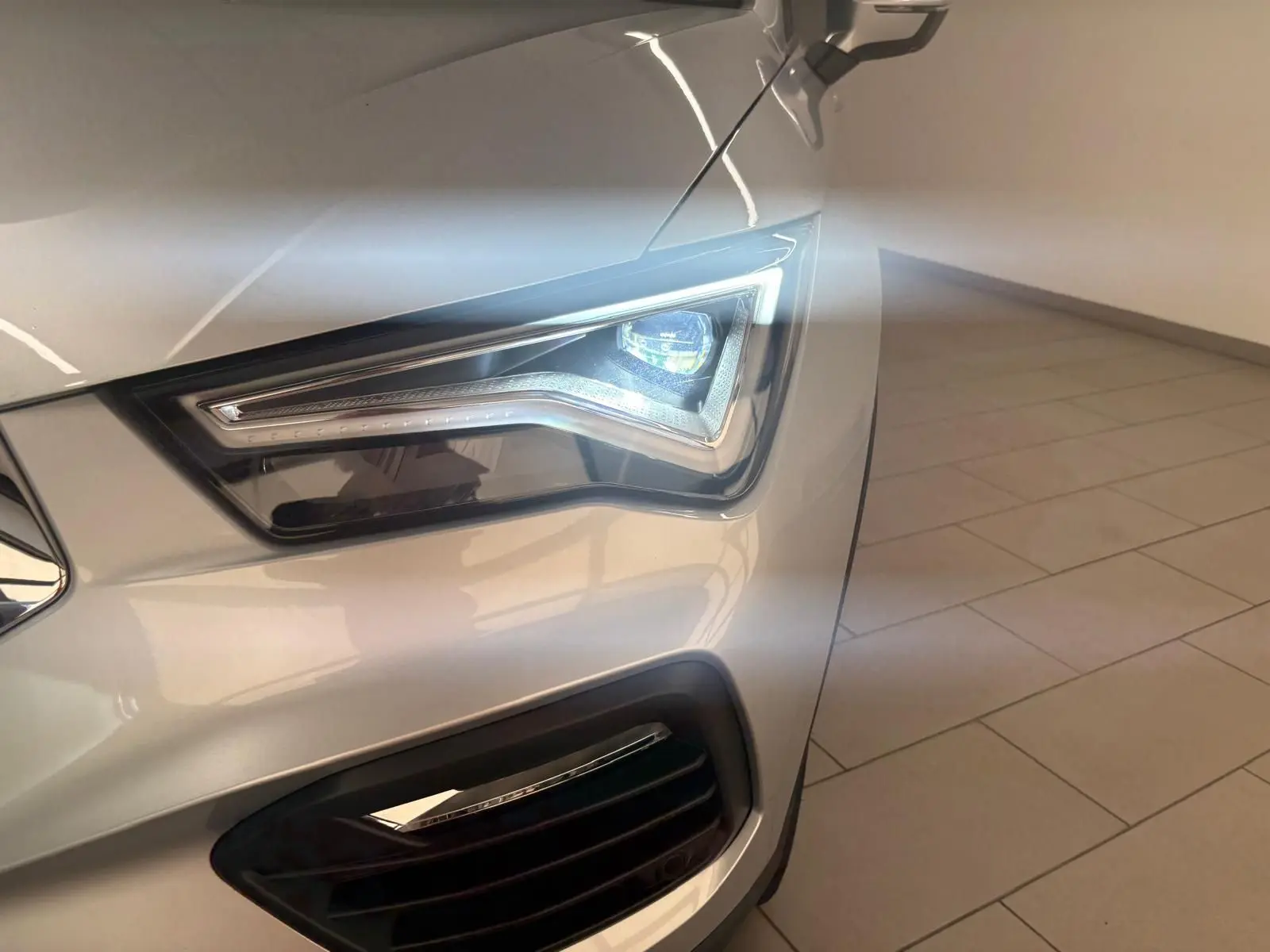 Gros plan sur le phare avant droit allumé d’un SEAT Ateca 2.0 TDI 150 DSG7 Copa en Argent Reflex métallisé.