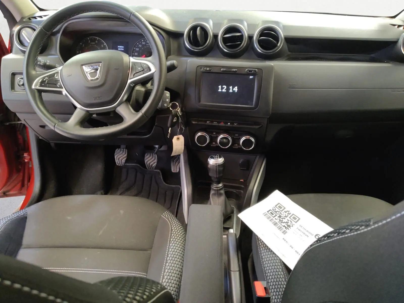 Vue intérieure avant du Dacia Duster rouge fusion 2021, montrant le volant, la console centrale avec écran tactile et levier de vitesses manuel.