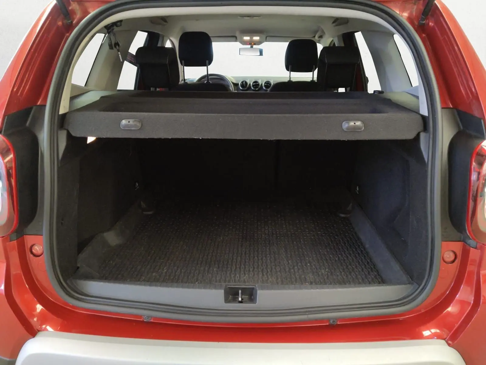 Coffre ouvert vu de l'arrière d'un Dacia Duster rouge fusion 2021, avec cache-bagages en place et intérieur noir.