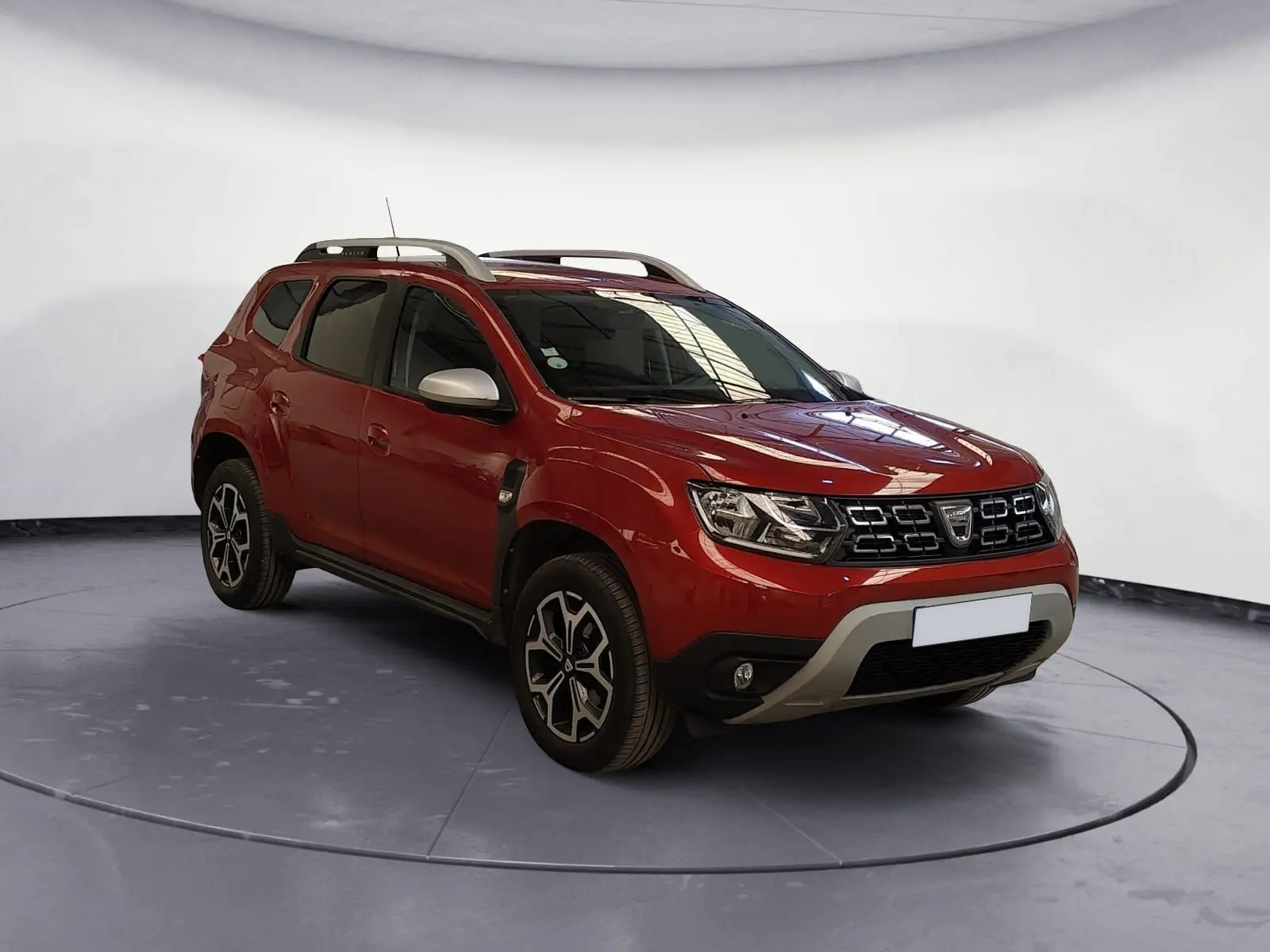 Dacia Duster rouge fusion en 3/4 avant droit, avec jantes alliage noires et barres de toit argentées.