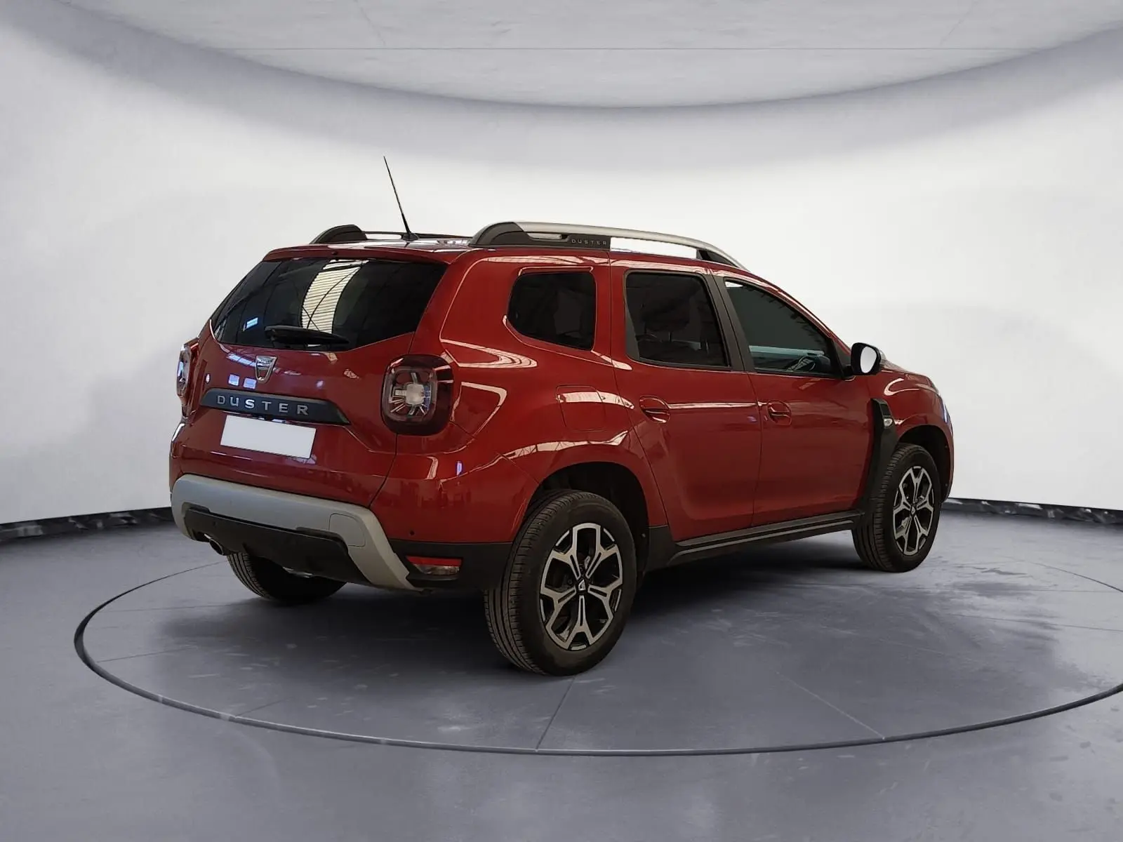 Dacia Duster rouge fusion en 3/4 arrière droit, avec barres de toit noires et jantes alliage 17 pouces.