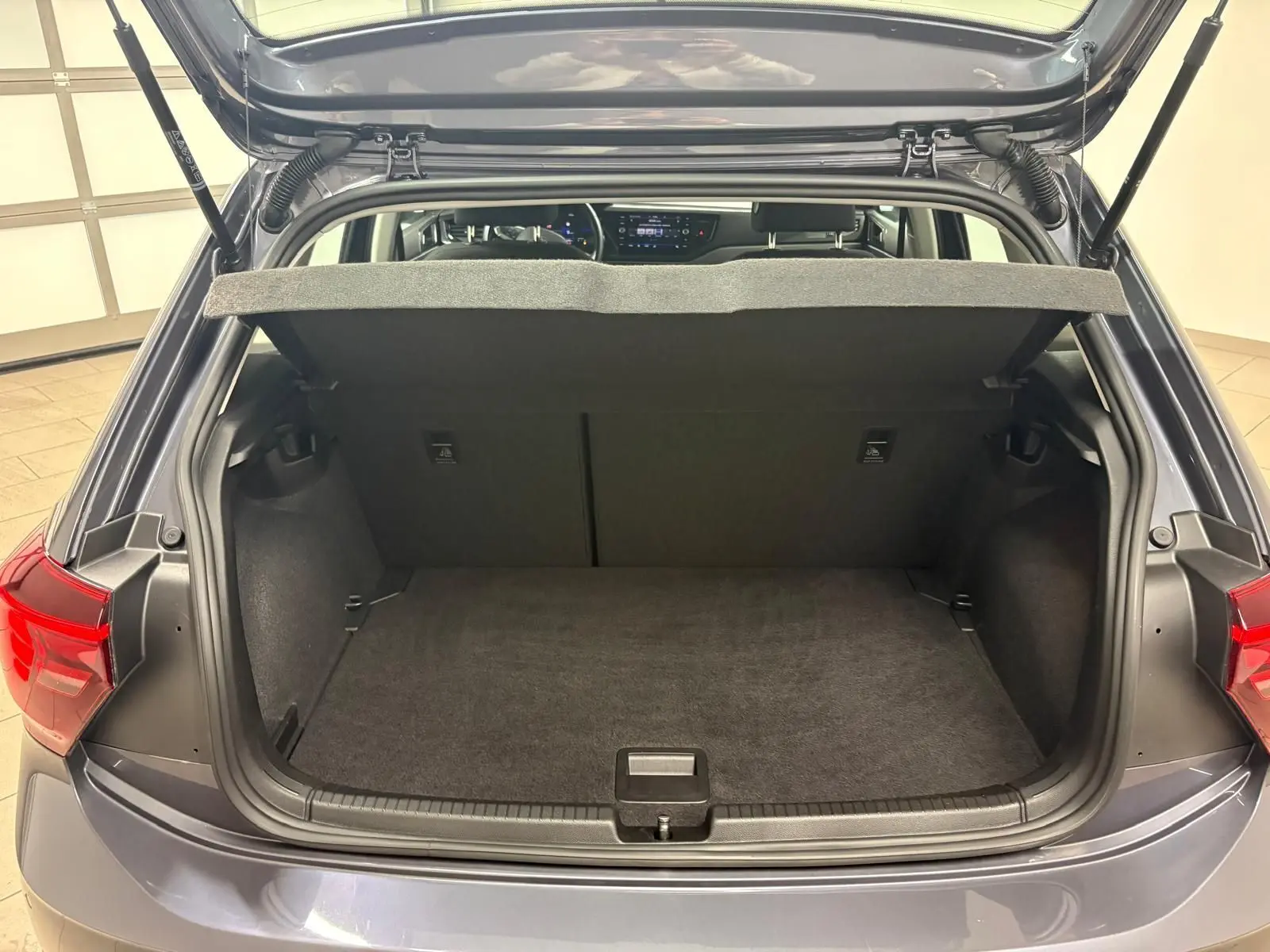 Vue arrière du coffre ouvert d'une Volkswagen Polo gris cendre 2024, montrant l'espace de chargement et la tablette arrière.