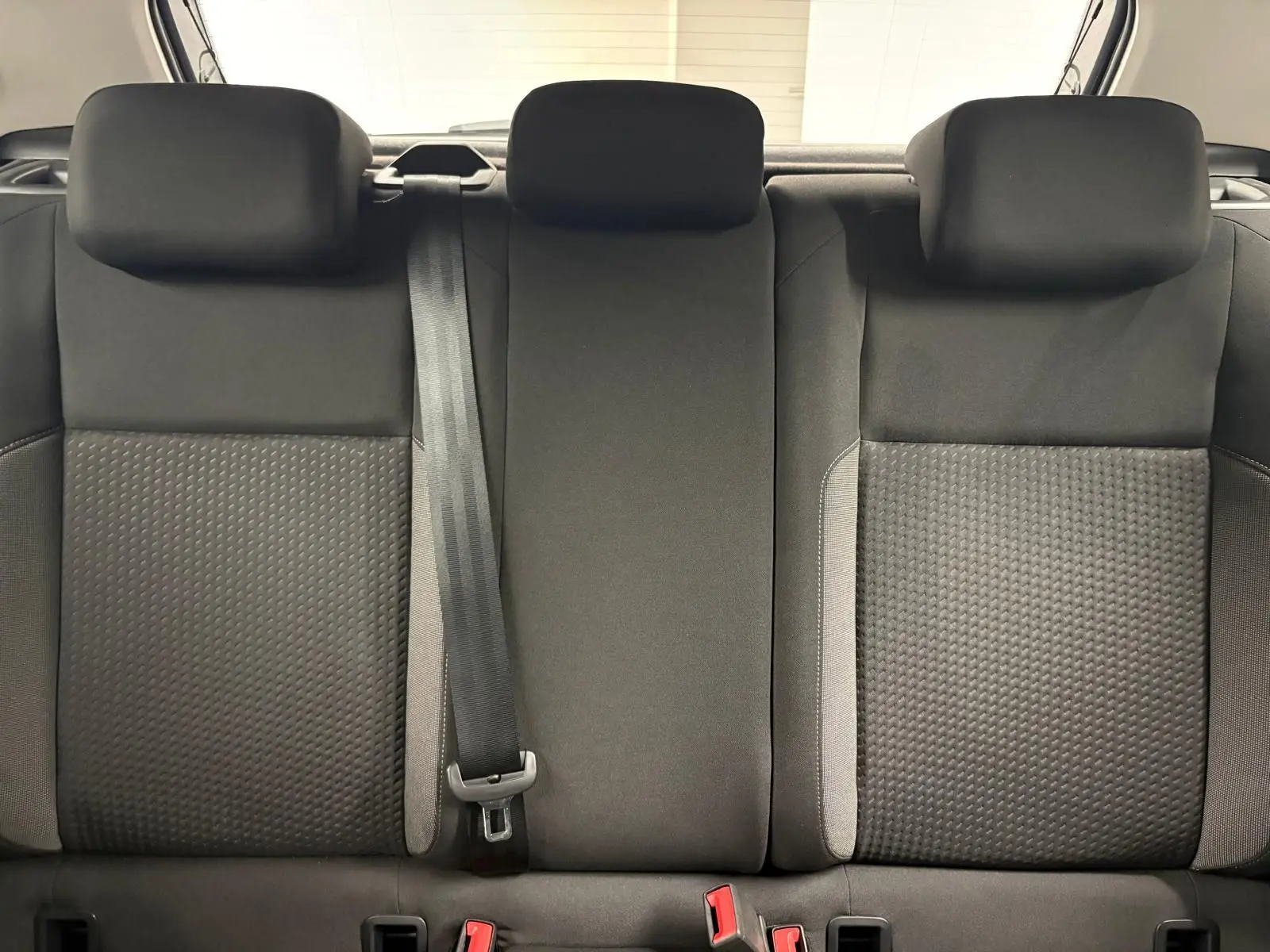 Vue rapprochée des sièges arrière noirs avec appuie-têtes et ceinture de sécurité centrale d'une Volkswagen Polo gris cendre 2024.