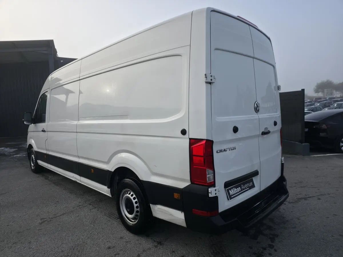 Vue 3/4 arrière droite d'un Volkswagen Crafter fourgon blanc avec jantes acier et bande noire latérale.
