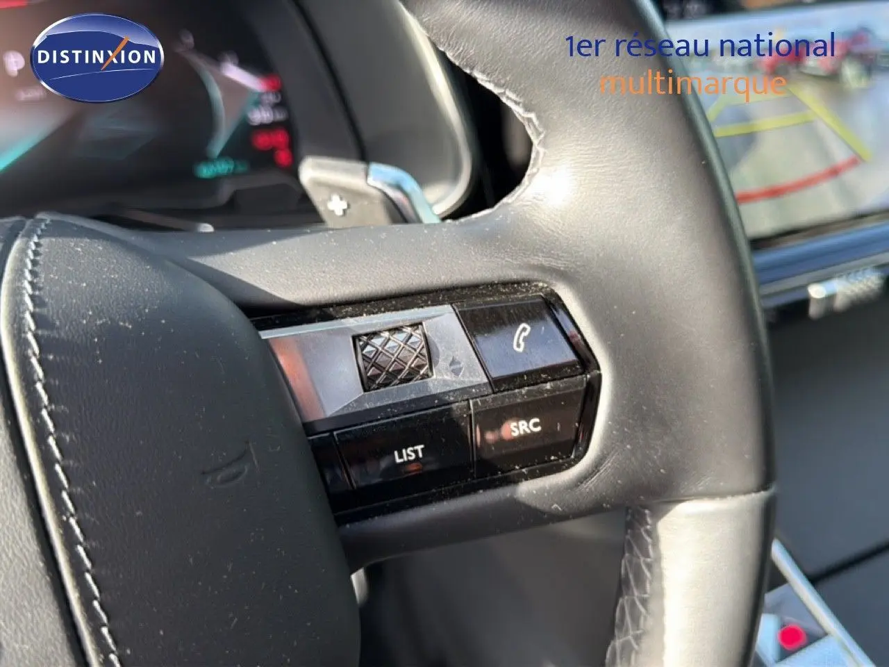 Gros plan sur les commandes au volant en cuir noir du DS7 1.5 BLUEHDI 130 EAT8 RIVOLI 2024, avec écran tactile en arrière-plan.