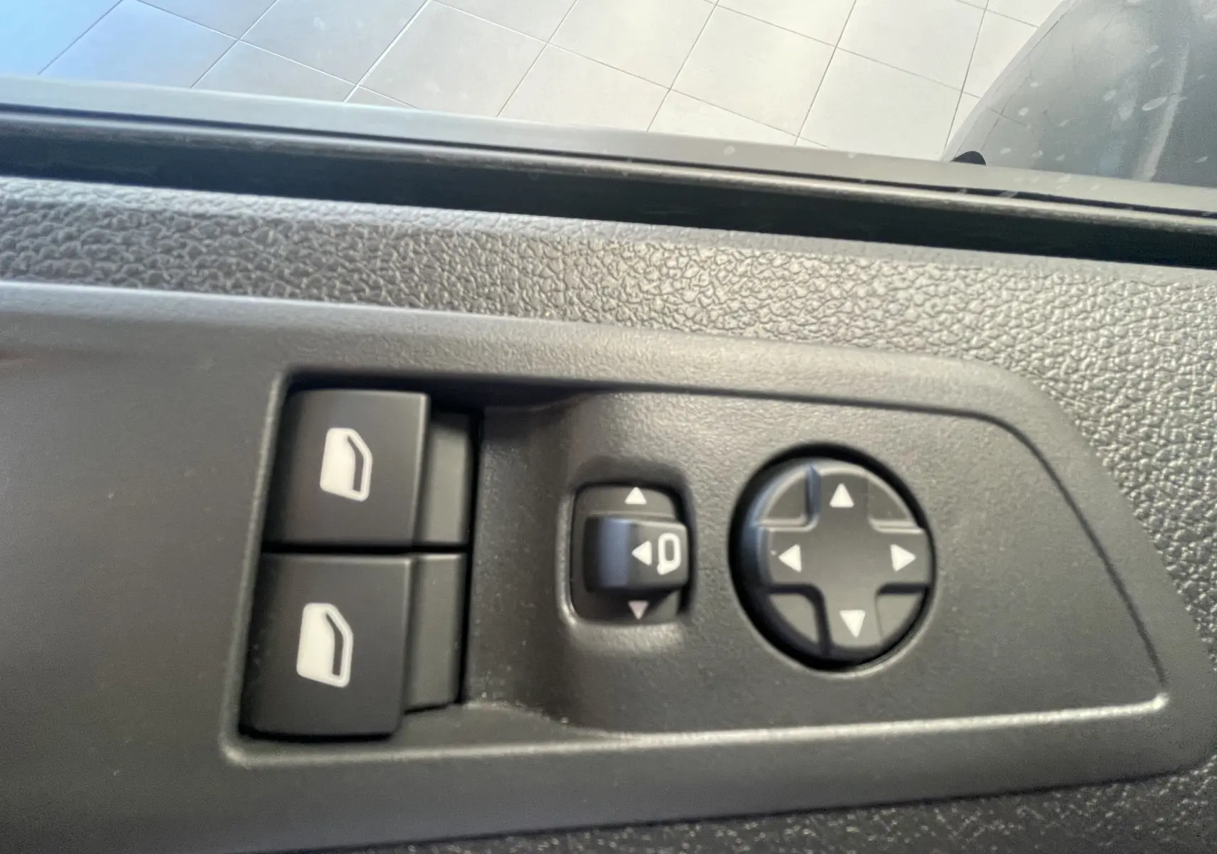 Gros plan sur les commandes de réglage des vitres et des rétroviseurs côté conducteur du Peugeot Traveller noir 2026.