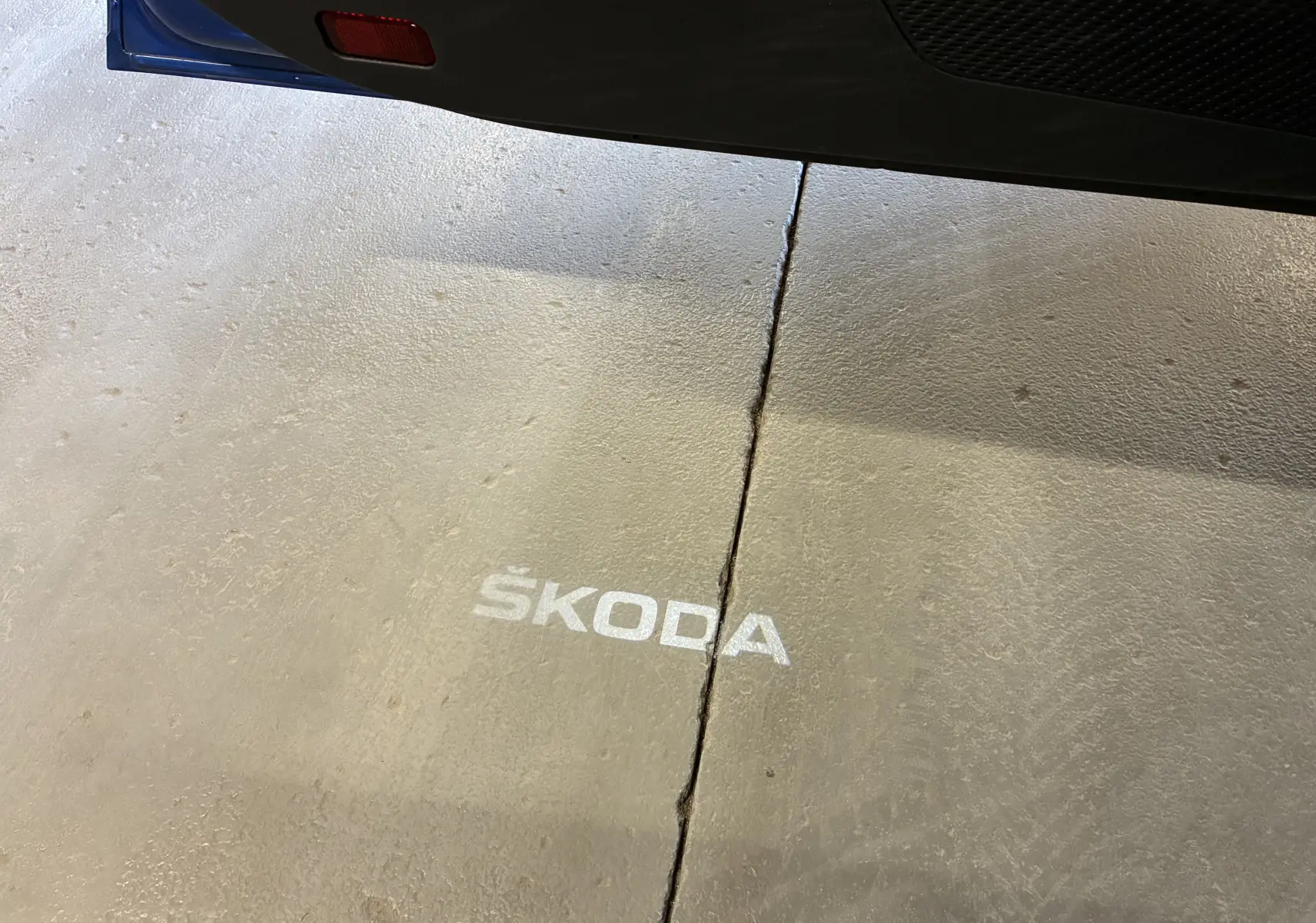 Projection lumineuse du logo SKODA au sol visible sous la porte ouverte d'une Octavia Combi bleue.