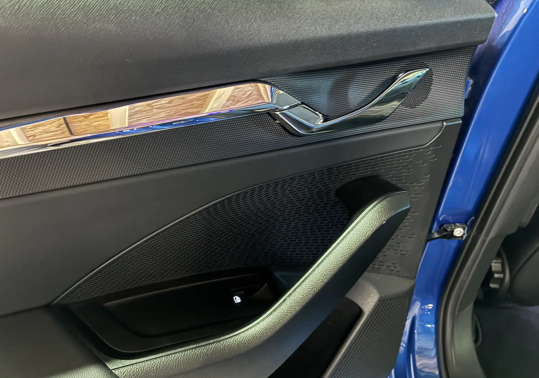 Détail de la porte avant gauche d’une Skoda Octavia Combi 2024 bleu, avec poignée intérieure chromée et bouton de verrouillage.
