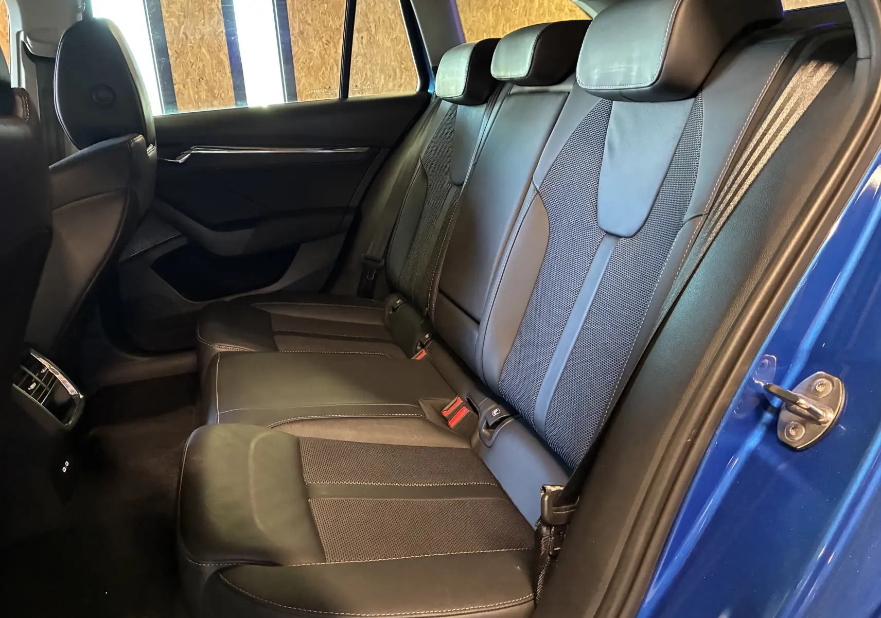Vue intérieure arrière droite de la Skoda Octavia Combi bleu 2024, sièges en tissu noir avec surpiqûres contrastées.