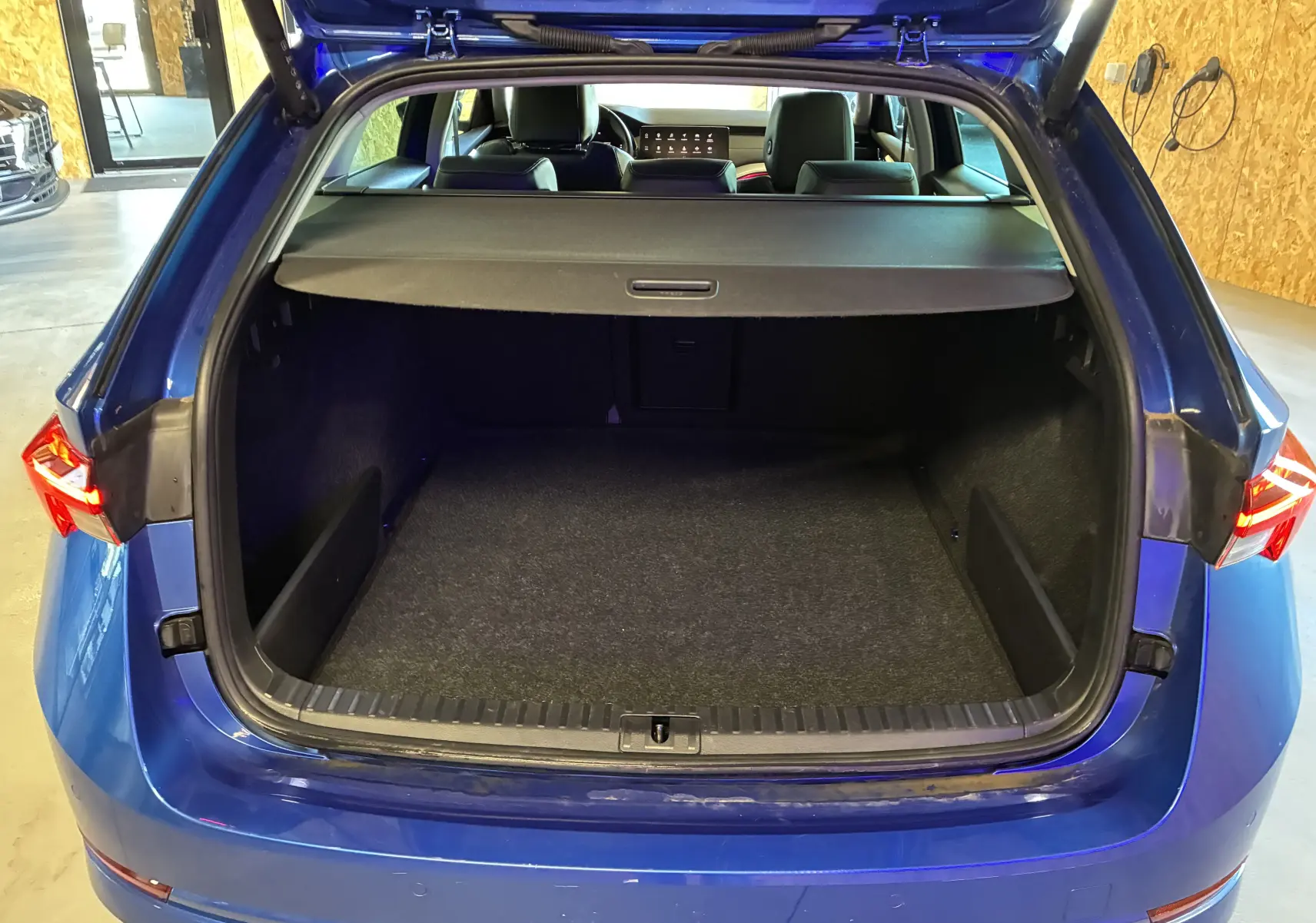 Vue arrière ouverte du coffre spacieux d'une Skoda Octavia Combi 2024 bleu, avec cache-bagages et intérieur noir visible.