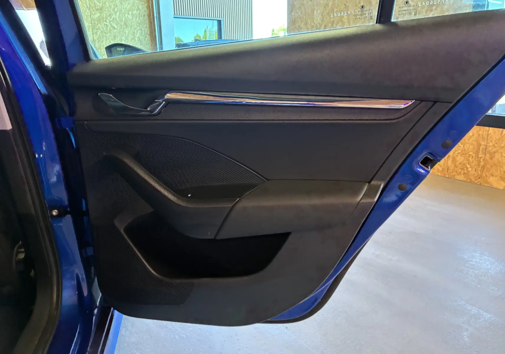 Vue rapprochée de la porte arrière gauche bleu foncé du Skoda Octavia Combi 2024 avec garniture intérieure noire et insert chromé.